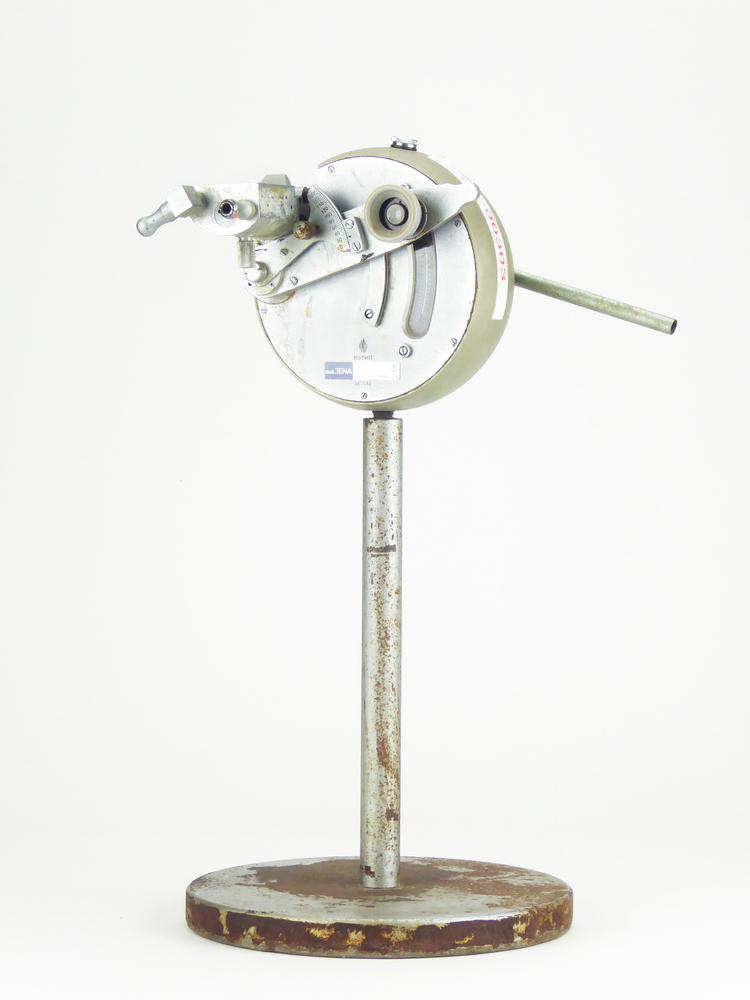 Refraktiemeter uit het voormalig Semi - Technisch Laboratorium van DWM te Veendam. Metalen ronde voet met opstaande metalen staaf waaraan ronde behuizing met aan voorkant kijkglas, in hoogte verstelbaar en scherp te stellen, links daarvan verschuifbare schaalverdeling, aan achterkant verstelbare metalen staaf met daarin glazen staafje met schaalverdeling (afgebroken), lamp mist. Met dit apparaat kan de hoeveelheid opgeloste zetmeel in een oplossing worden gemeten, de zgn refraktie. Er wordt een druppel van de oplossing tussen twee spiegels geplaatst en m.b.v. een lamp is dan een scheidingslijn te zien. Die scheidingslijn komt overeen met een getal op de meter en is de refraktie. Refraktie wordt uitgedrukt in graden Brix.