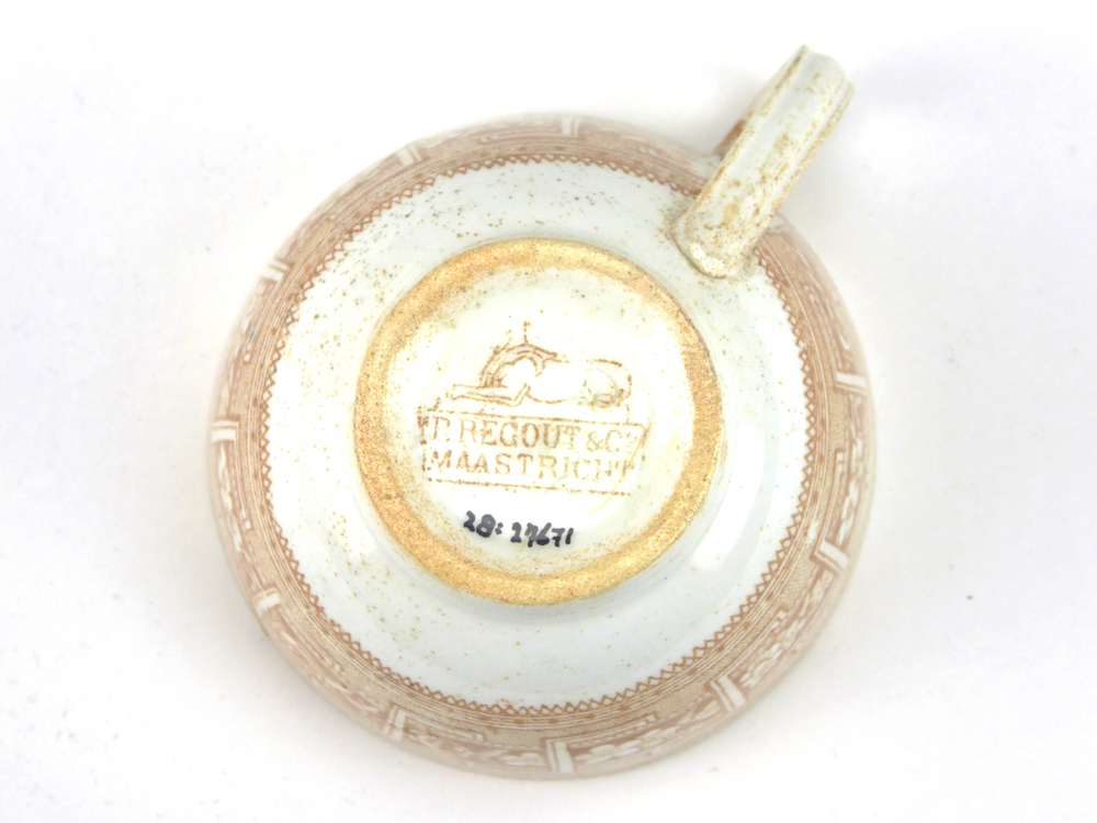 aardewerken kop van het merk Petrus Regout & Co, Maastricht, diameter 8,2 cm, op buitenkant bruine decoratie van bloemen en gestileerde wolfsangel, gemerkt met beeldmerk 71 A van Petrus Regout, opgedoken door British Sub Aqua Club, Branch 501, ook wel de 501 Divers uit Folkstone, uit het wrak van de op 19 november 1887 na een aanvaring met het stoomschip Rosa Mary gezonken stoomschip W.A. Scholten, via hun woordvoerder Glyn Jones geschonken aan het Veenkoloniaal Museum.