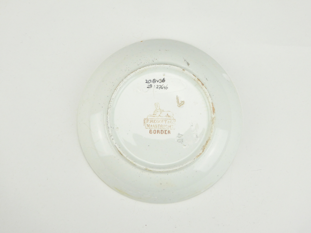 aardewerken schotel van het merk Petrus Regout & Co, Maastricht, decornaam Border, diameter 13,5 cm, op binnenkant bruine decoratie van bloemen en wolfsangel, gemerkt met beeldmerk 71 A van Petrus Regout, blindmerk 4 en AV, opgedoken door British Sub Aqua Club, Branch 501, ook wel de 501 Divers uit Folkstone, uit het wrak van de op 19 november 1887 na een aanvaring met het stoomschip Rosa Mary gezonken stoomschip W.A. Scholten, via hun woordvoerder Glyn Jones geschonken aan het Veenkoloniaal Museum.