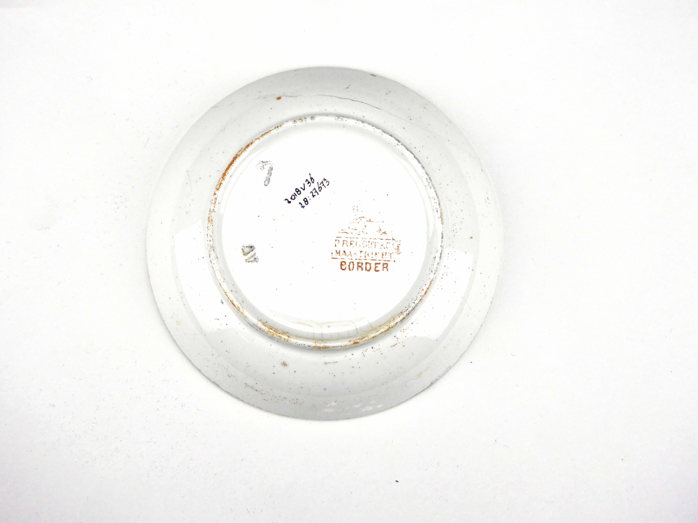aardewerken schotel van het merk Petrus Regout & Co, Maastricht, decornaam Border, diameter 13,4 cm, op binnenkant bruine decoratie van bloemen en wolfsangel, gemerkt met beeldmerk 71 A van Petrus Regout, opgedoken door British Sub Aqua Club, Branch 501, ook wel de 501 Divers uit Folkstone, uit het wrak van de op 19 november 1887 na een aanvaring met het stoomschip Rosa Mary gezonken stoomschip W.A. Scholten, via hun woordvoerder Glyn Jones geschonken aan het Veenkoloniaal Museum.