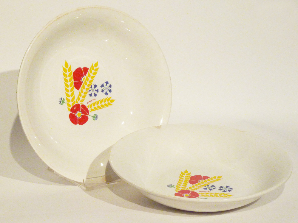 diep aardewerken bord met  afbeelding twee rode en twee blauwe bloemen , drie gele korenaren en rode belettering Brinta