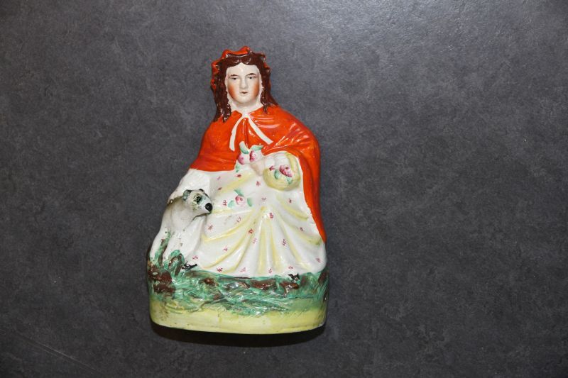 Victoriaans beeldje van een vrouw met oranje cape met gebloemde jurk en bloemen, rechts naast haar een dier, roodkapje en de wolf