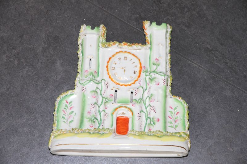 kasteel met twee torens met kantelen waartussen ronde geschilderde wijzerplaat in relief druivenranken geel oranje enig goud en bietenrood gleuven als ramen op basis met gouden biesje