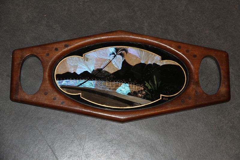 langwerpige dienblad met hoekige boven- en onderkant met in het midden glasschildering van een gezicht op de baai te Rio de janeiro met op voorgrond en straat, alles in het zwart, groen en goud, opgevuld met vlindervleugels